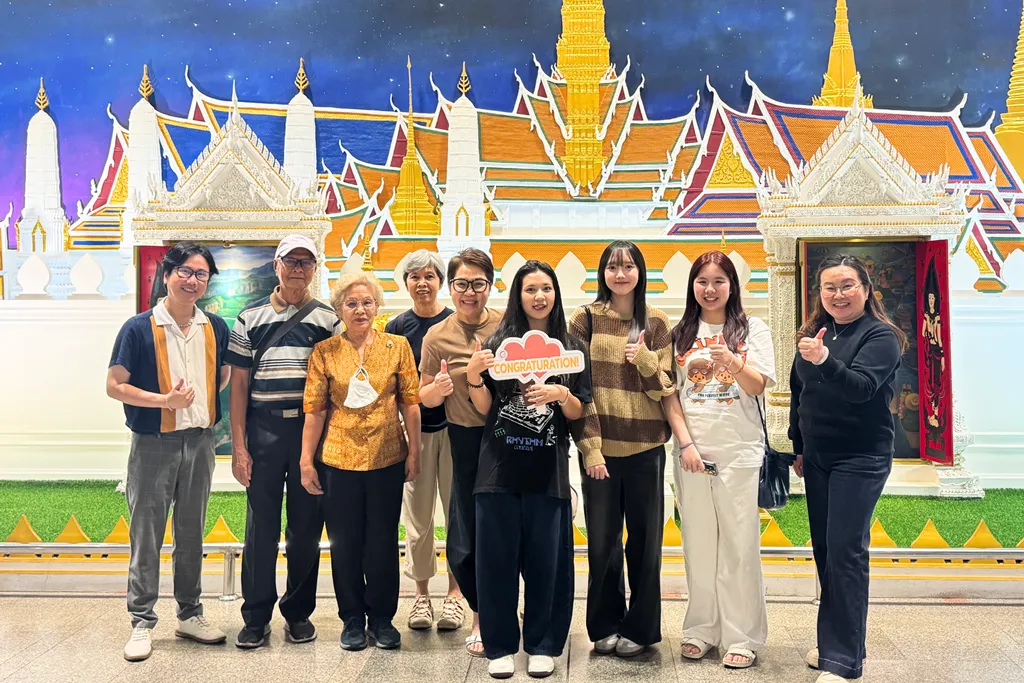 นักเรียนไทยและครอบครัวถ่ายภาพหมู่หน้าฉากศิลปะไทย พร้อมป้ายแสดงความยินดี