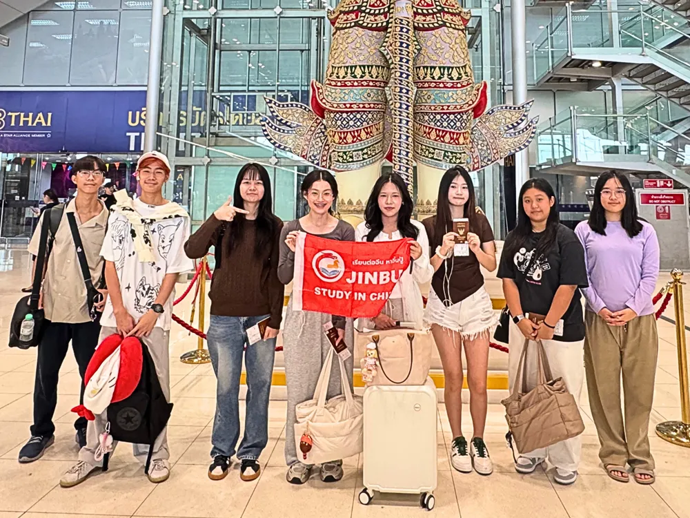 นักเรียนไทยกลุ่มเล็กถ่ายภาพหน้ารูปปั้นยักษ์สนามบินสุวรรณภูมิ ถือป้าย Jinbu Study in China ก่อนเดินทางเข้าร่วมโครงการ Live & Learn in China