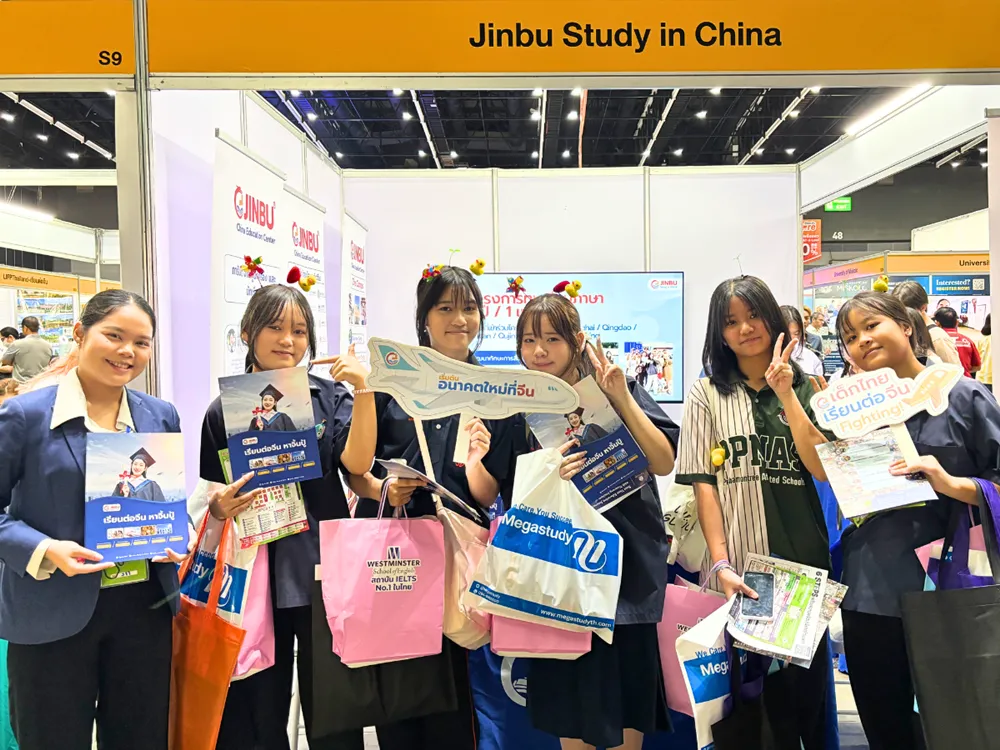นักเรียนไทยถ่ายภาพหน้าบูธ Jinbu Study in China ในงานนิทรรศการ ถือเอกสารและป้ายประชาสัมพันธ์