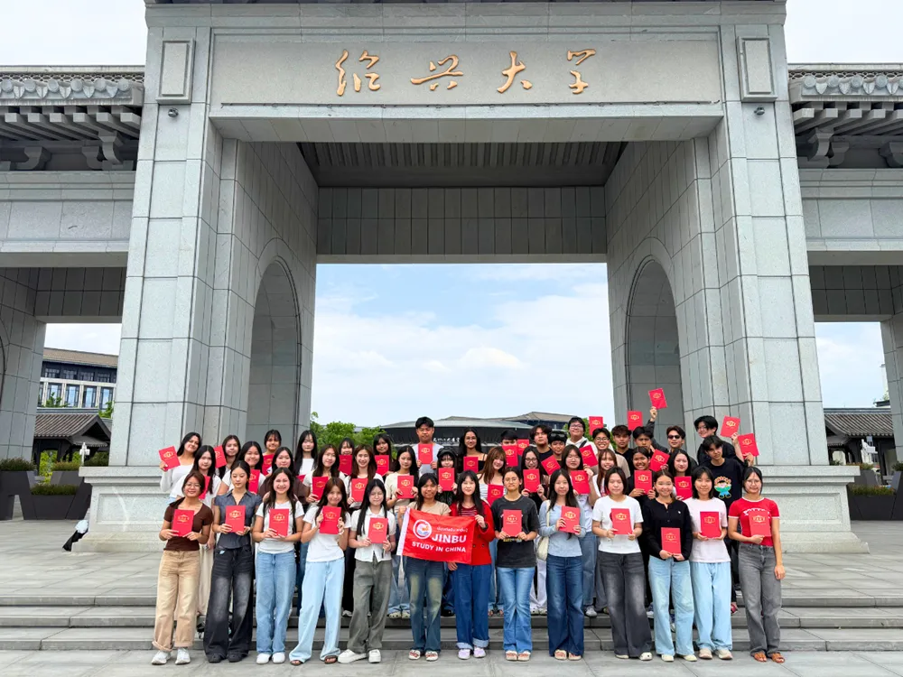 นักเรียนไทยถือประกาศนียบัตรและแบนเนอร์ Jinbu Study in China หน้าประตูหินใหญ่ในจีน รอบมีนาคม–เมษายน 2569
