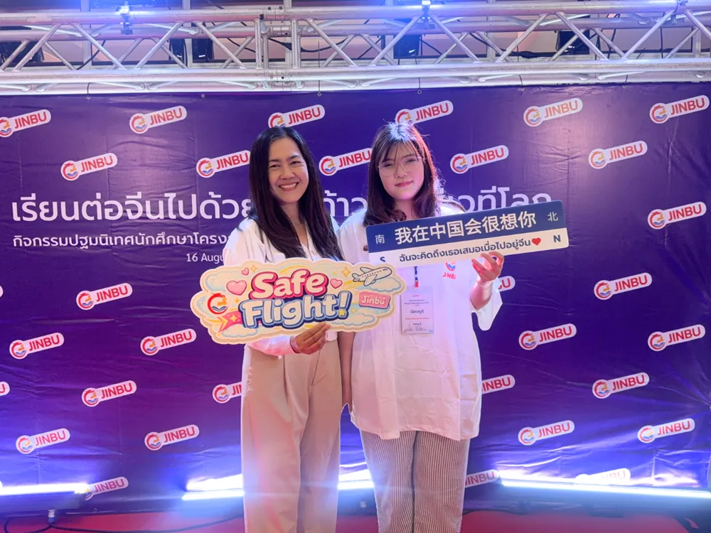 นักศึกษาถ่ายภาพกับป้ายกิจกรรมปฐมนิเทศ Jinbu พร้อมข้อความอวยพร Safe Flight