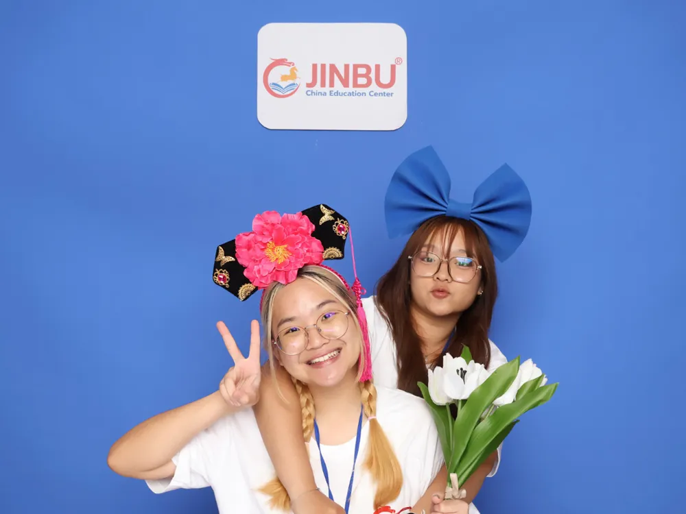 นักศึกษาสวมเครื่องประดับดอกไม้และถือช่อดอกไม้ ถ่ายภาพหน้าป้าย Jinbu China Education Center