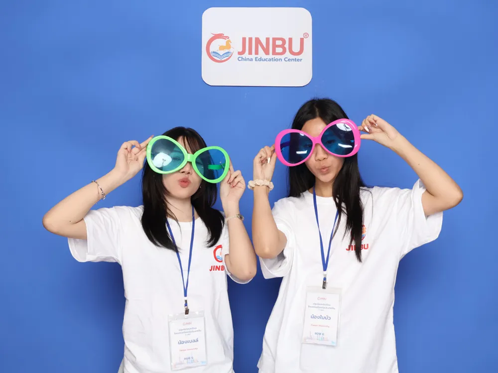 นักศึกษาสวมแว่นตาแฟนซีสีเขียวและชมพู ถ่ายภาพหน้าป้าย Jinbu China Education Center