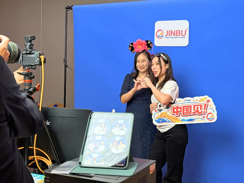 นักศึกษาถ่ายภาพกับป้าย Jinbu China Education Center พร้อมข้อความ 中国见! See you in China
