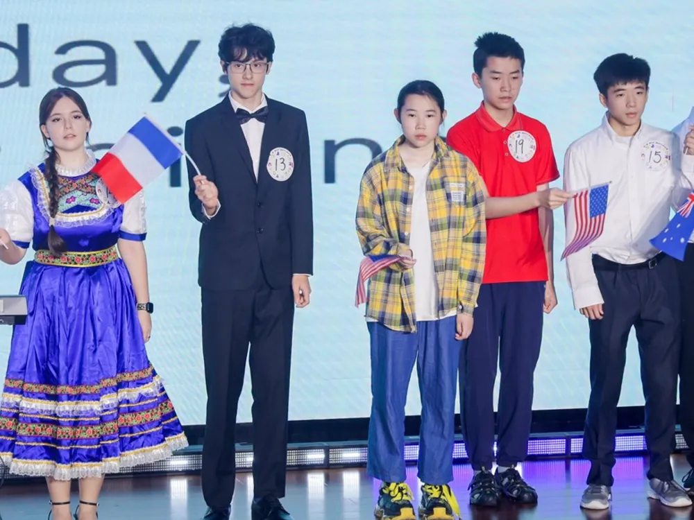 ผู้เข้าร่วมถือธงชาติฝรั่งเศส อเมริกา และออสเตรเลียบนเวทีงานแข่งขันสุนทรพจน์