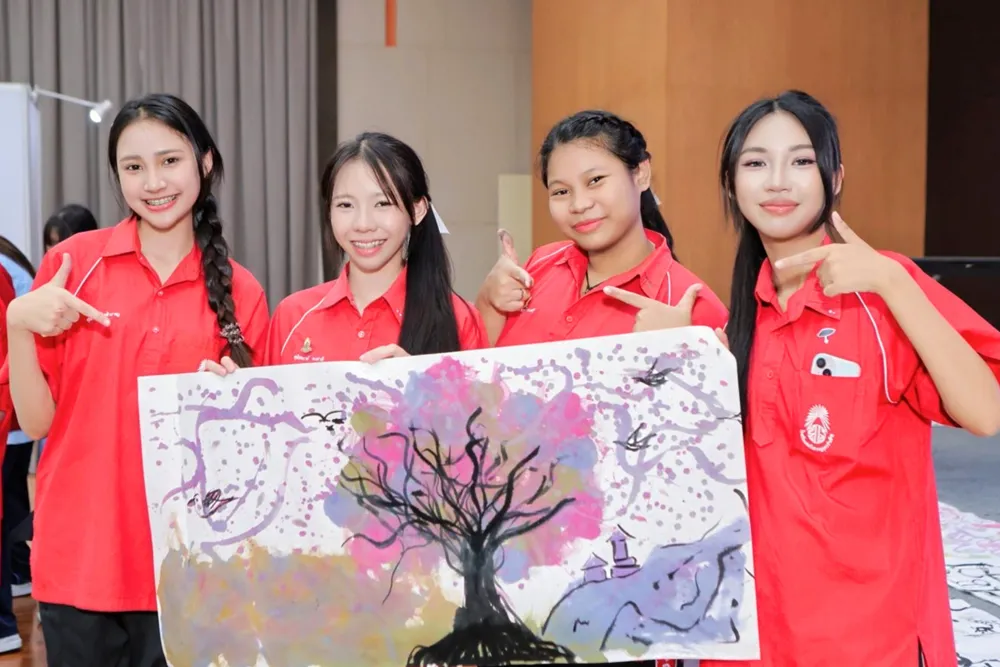 นักเรียนสวมเสื้อสีแดงร่วมสร้างสรรค์ภาพวาดต้นไม้ในกิจกรรมศิลปะอักษรจีน